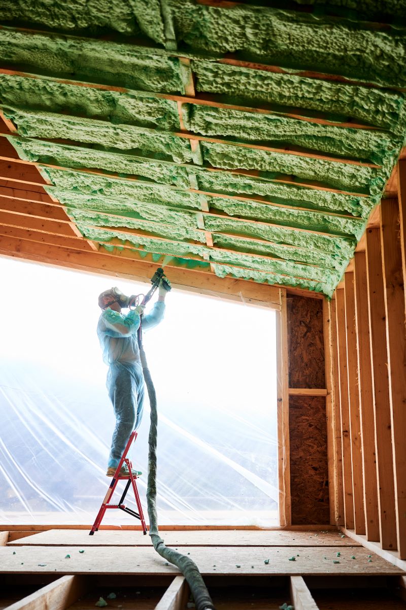 Worker spraying polyurethane foam insulation inside of commercial building